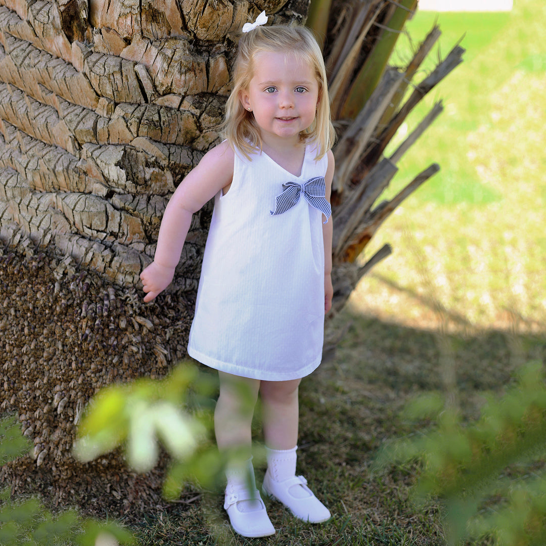 Young girl in a white dress with a bow standing next to a tree