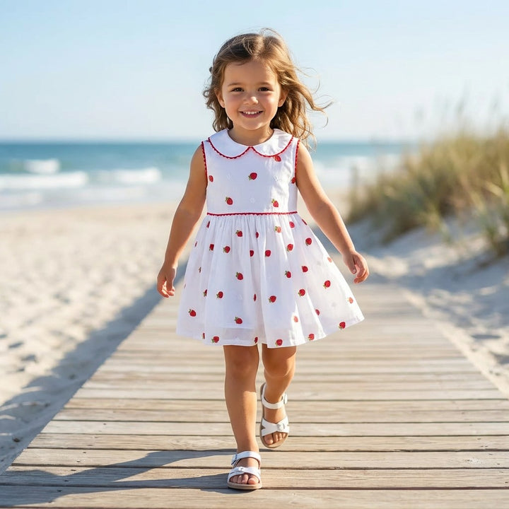 Young girl in a white dress with red strawberries walking on a wooden boardwalk at the beach.