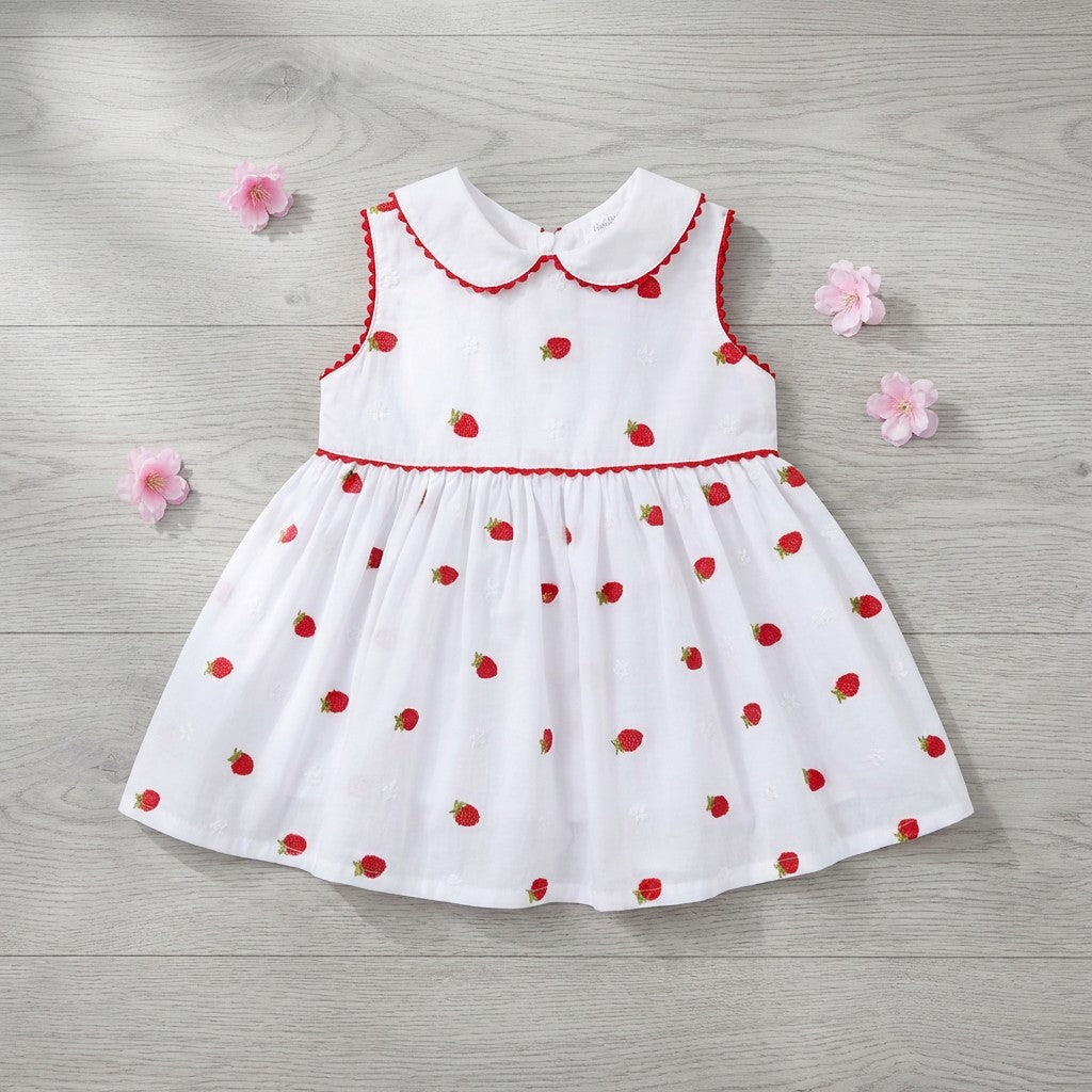 White dress with red strawberry pattern on a wooden surface with pink flowers.