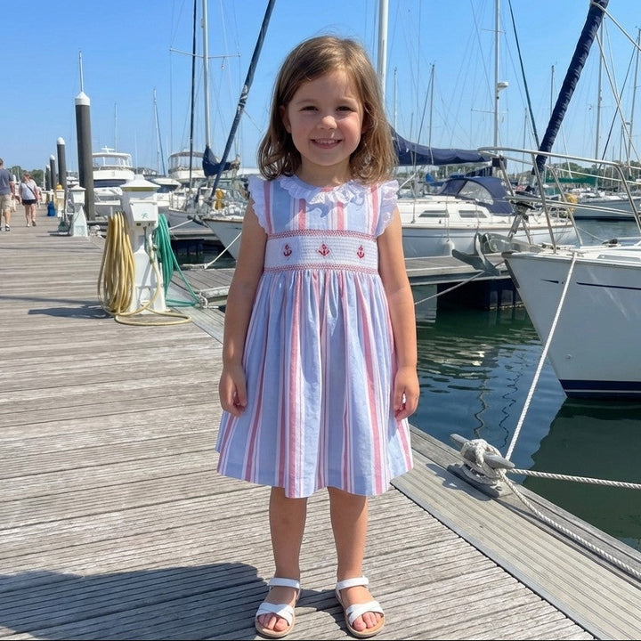 Young girl in a striped dress standing on a dock with boats in the background