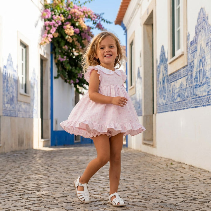 Young girl in a pink dress standing on a cobblestone street with decorative tiles and flowers.
