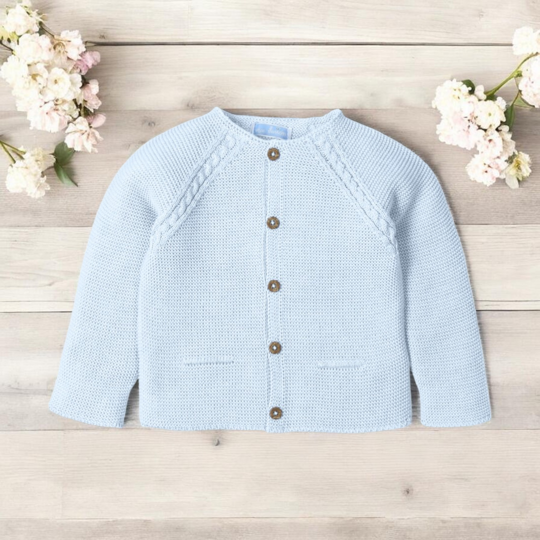 Light blue knitted cardigan on a wooden surface with white flowers.