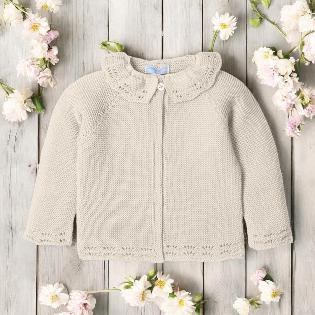 Knitted baby cardigan on a wooden surface with flowers around