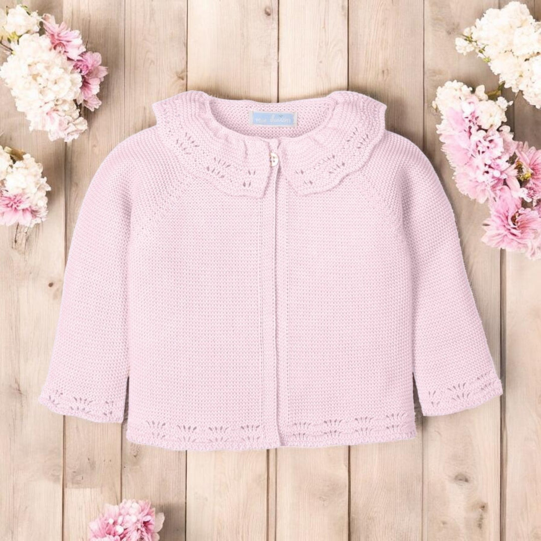 Pink knitted cardigan on a wooden surface with flowers around