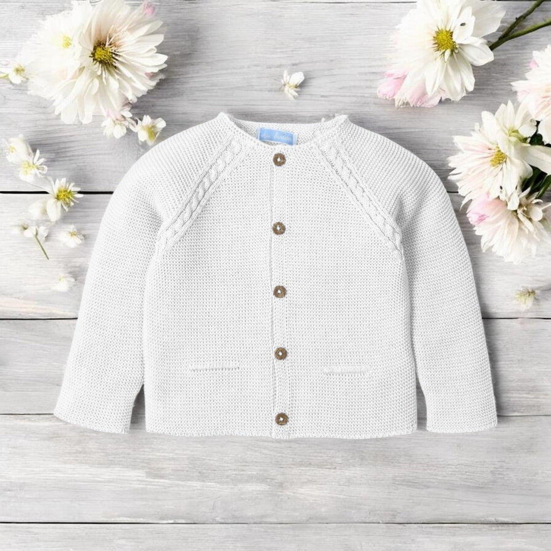 White baby cardigan on a wooden surface with flowers around