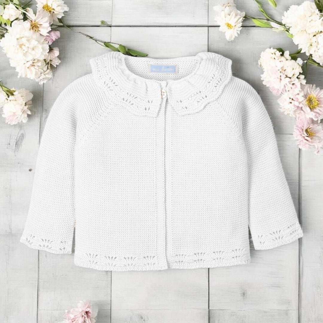 White babycardigan on a light wooden surface with flowers around