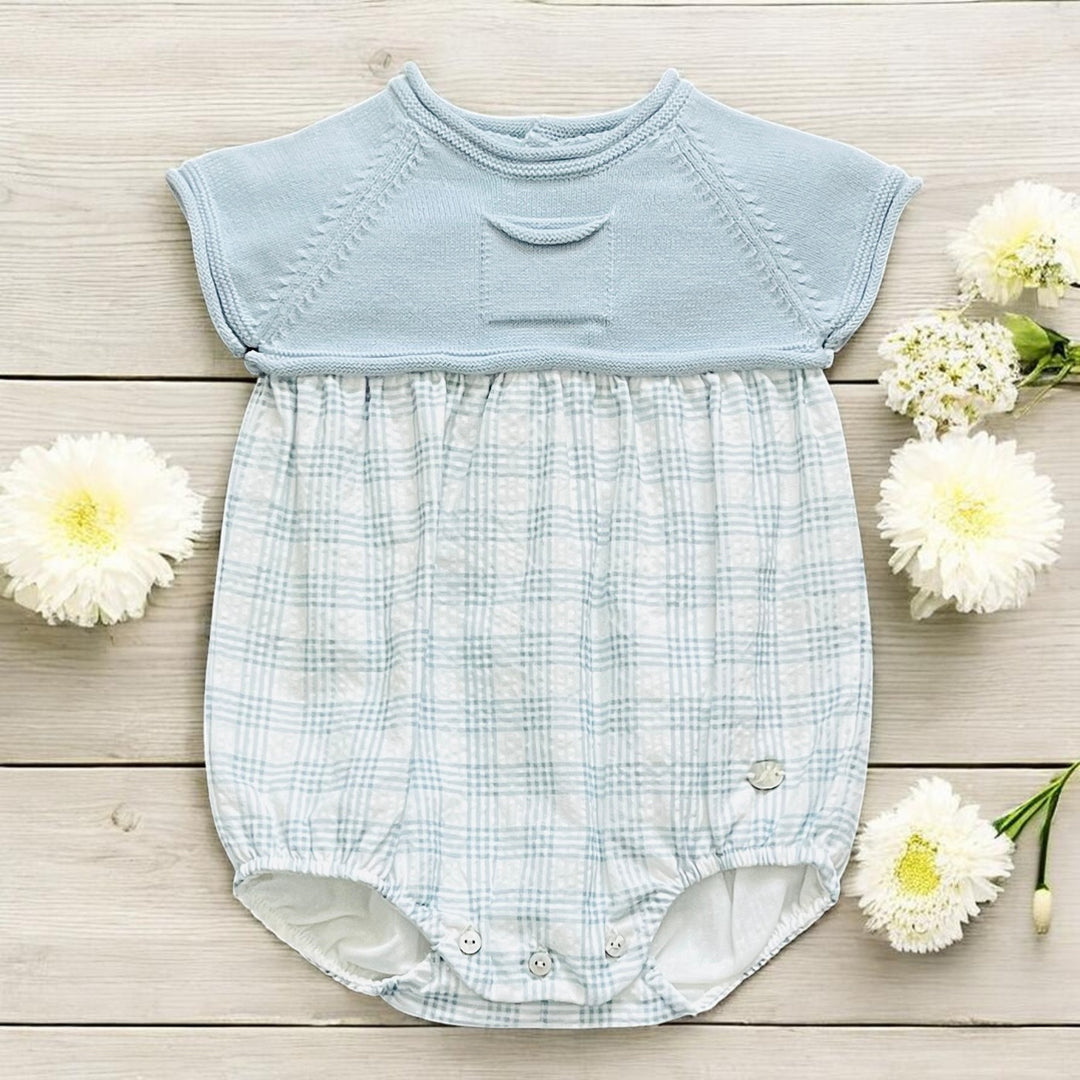 Light blue baby romper with checkered pattern on a wooden surface with white flowers.