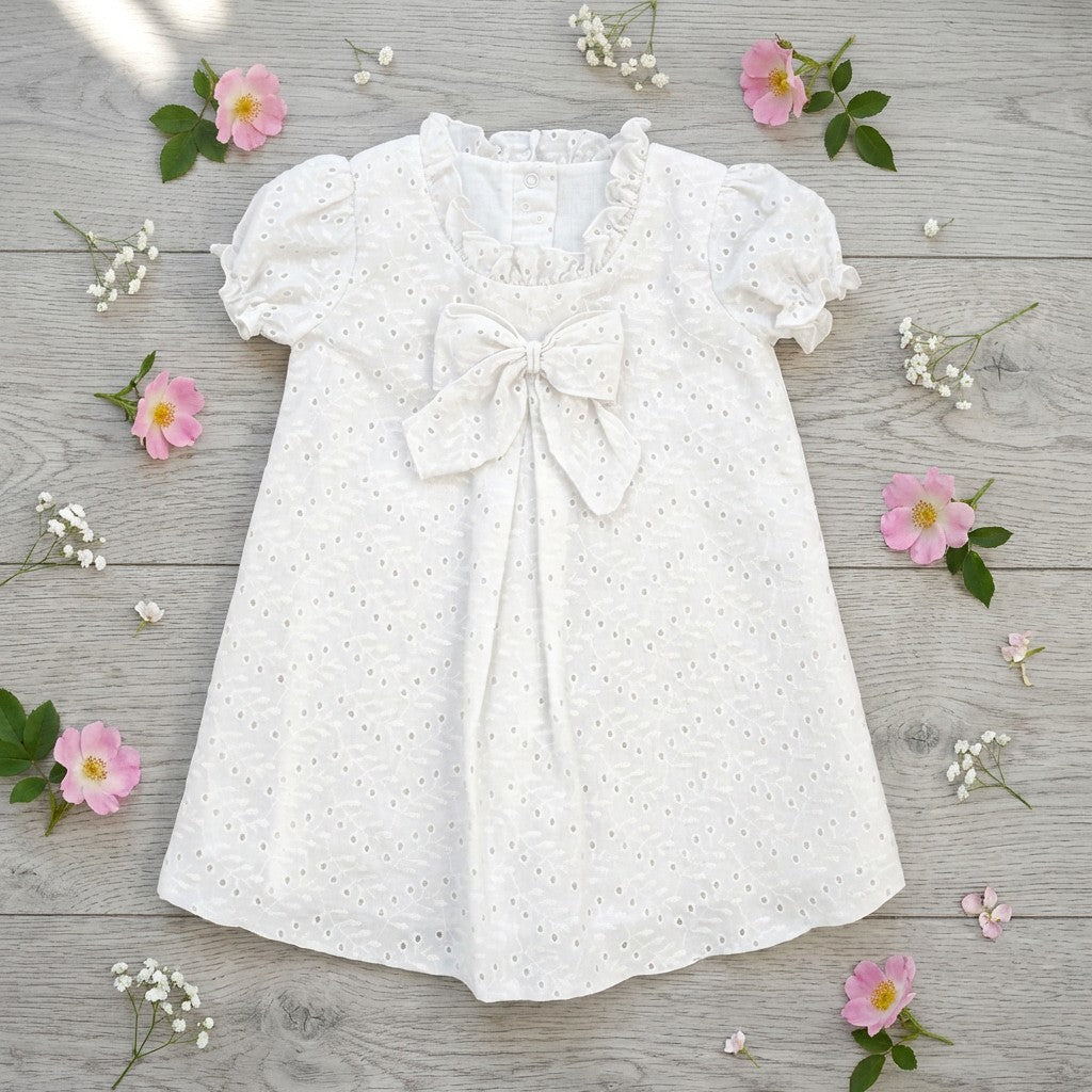 White baby dress with a bow on a wooden surface with pink flowers