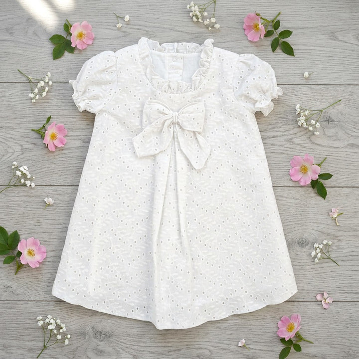 White baby dress with a bow on a wooden surface with pink flowers